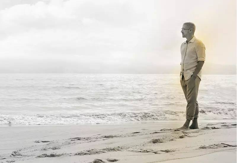 Male walking barefoot along beach wearing glasses 